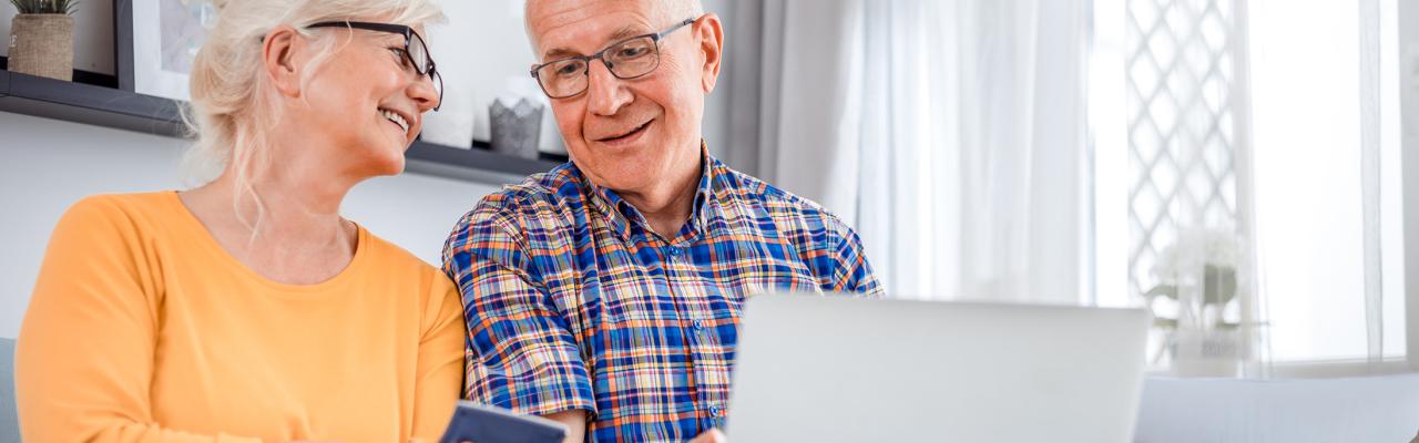 two older adults smile using their phone and laptop